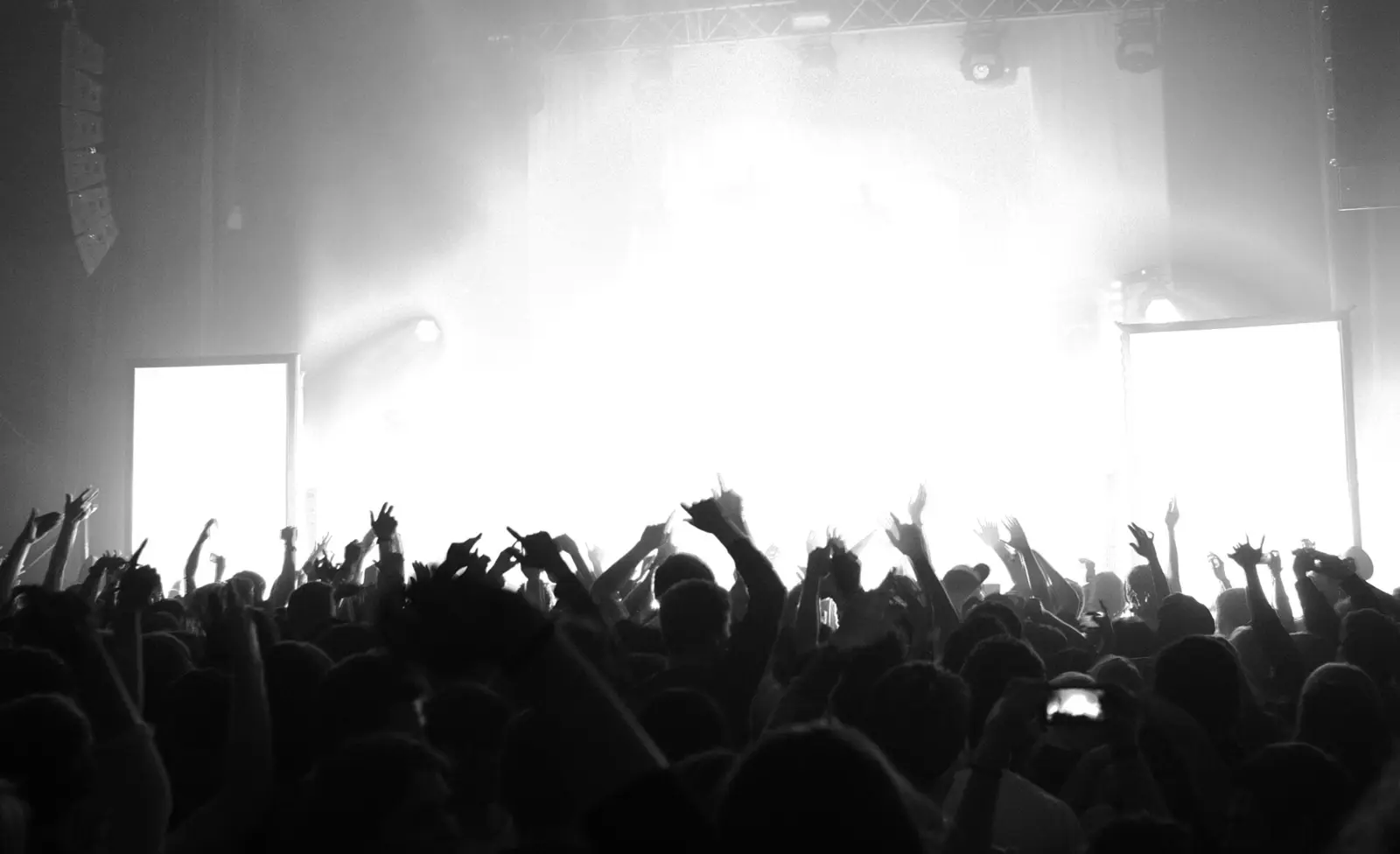 A crowd with hands in the air in front of a bright stage