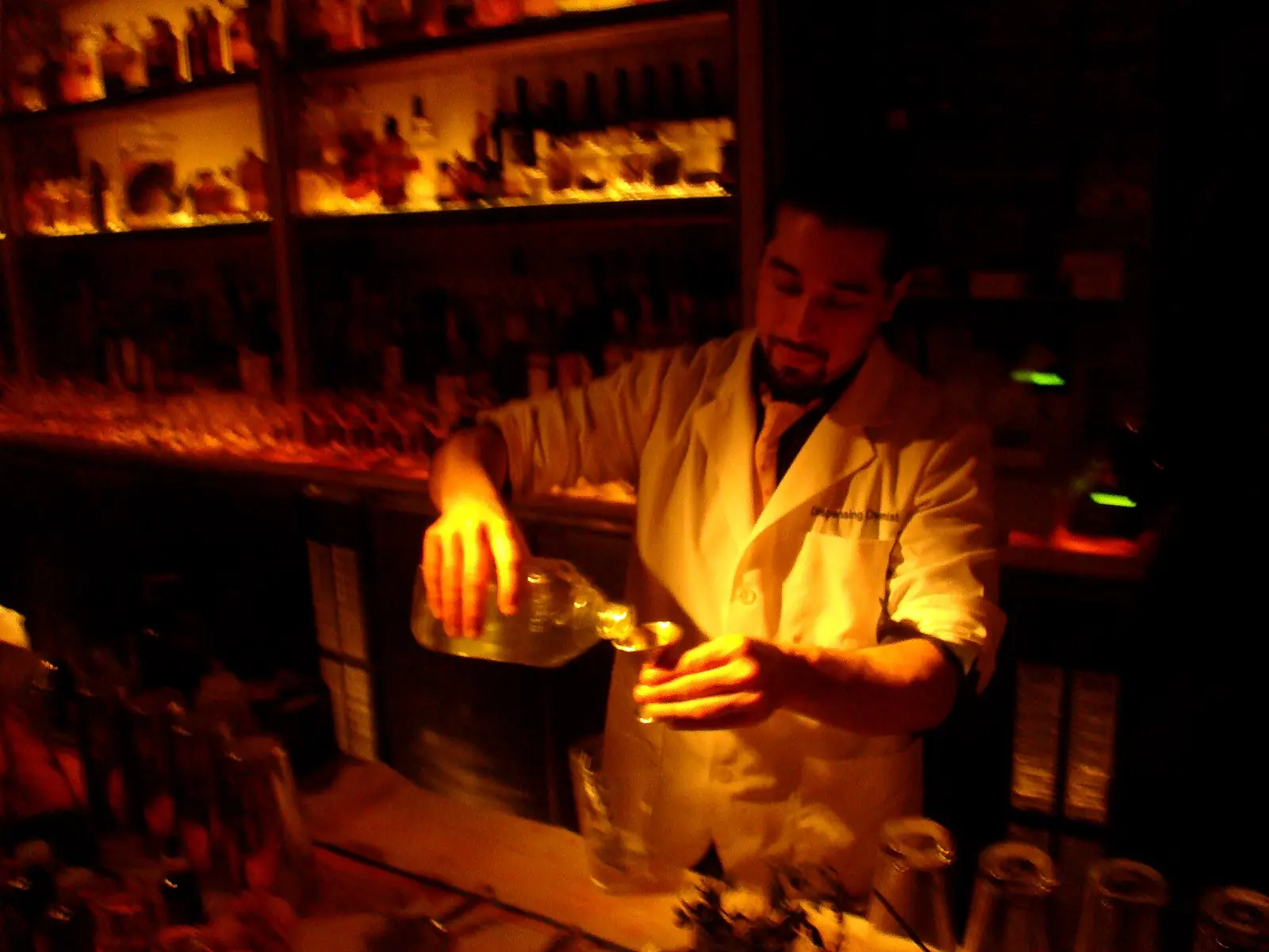 A bartender pouring a drink behind a warmly lit bar